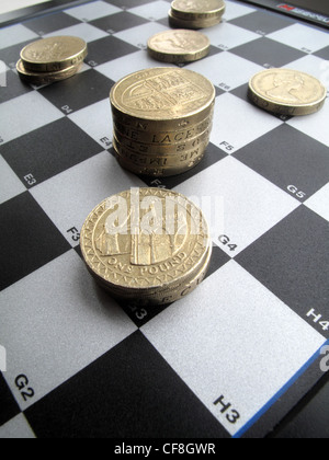 Impilate i quantitativi di British una libbra di monete di sedersi su un bianco e nero checkers , gioco di scacchi bordo. Foto Stock