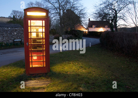 La luce da un tradizionale telefono rosso box si accende un colore scuro e lonely viottolo di campagna del Dorset villaggio di Cerne Abbas. Inghilterra, Regno Unito. Foto Stock
