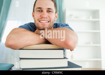 Studente sorridente appoggiato su una pila di libri Foto Stock