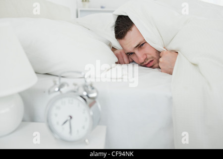 Uomo che copre le sue orecchie mentre la sua sveglia suona Foto Stock