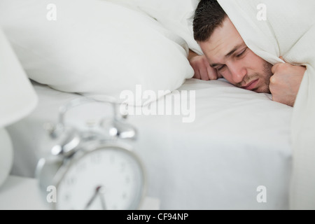 Giovane uomo che copre le sue orecchie mentre la sua sveglia suona Foto Stock