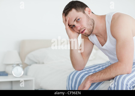 Uomo malato seduto sul suo letto Foto Stock