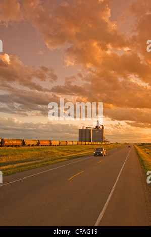 Strada attraversando le praterie e terrestri terminale di grano in background, vicino Estevan, Saskatchewan, Canada Foto Stock