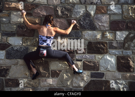 Una giovane donna di massi il suo modo sulla parete di un edificio in Canmore, Alberta, Canada. Foto Stock
