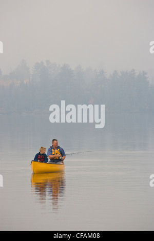 Giovani/uomo di mezza età pesca con il figlio dalla canoa sul lago di origine, Algonquin Provincial Park, Ontario, Canada. Foto Stock