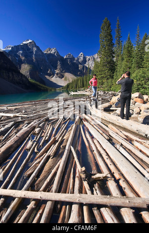 I turisti di scattare una foto su driftwood logs. Il Lago Moraine e Valle dei Dieci Picchi, il Parco Nazionale di Banff, Alberta, Canada. Foto Stock