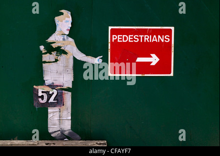 Freccia bianca su sfondo rosso per dirigere i pedoni intorno a Londra lavori stradali con dipinto di figura umana Foto Stock
