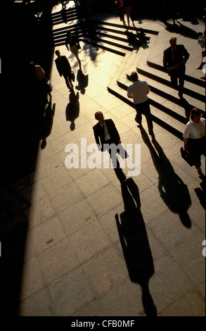 I pedoni a camminare in prima serata in tutta la plaza aperta a Broadgate con ombre cadendo dietro di loro, Londra, Regno Unito. Foto Stock