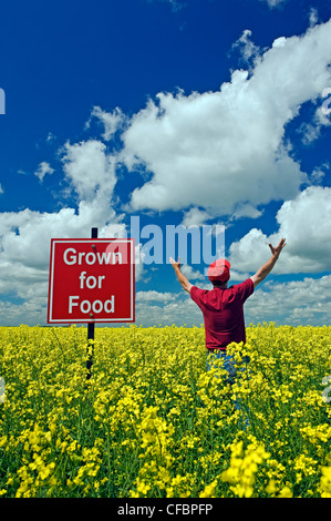 Un agricoltore si affaccia sulla sua fioritura di raccolto di canola con 'cresciuti per alimentare" segno nel campo vicino a Carey, Manitoba, Canada Foto Stock