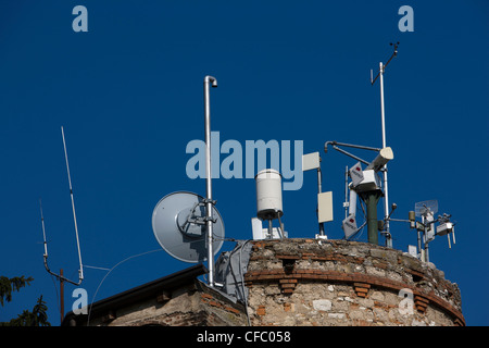 Schiera di antenne per telefonia mobile e antenne sulla parte superiore di una antica torre rotonda in Italia Foto Stock