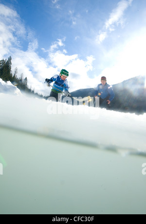 Un giovane ragazzo gioca pond hockey con un adulto skater pioppi neri americani sul lago, Nelson, British Columbia, Canada Foto Stock