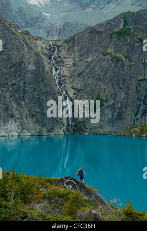 Una giovane donna escursioni nella parte anteriore di un lago azzurro e cascata nella gamma Niut, British Columbia, Canada Foto Stock