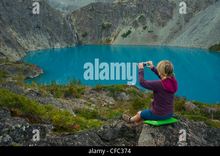 Una giovane donna scatta una foto di una cascata e il lago blu con un punto-e-shoot fotocamera, British Columbia, Canada Foto Stock