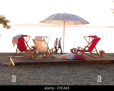 Tre sedie a sdraio e un ombrellone al tramonto, Feldwies beach, Chiemsee, Chiemgau, Baviera, Germania Foto Stock