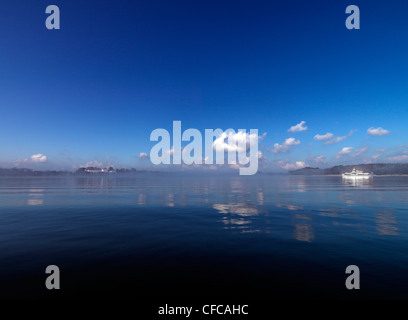 Vista attraverso la riflessione verso il lago Herreninsel, traghetto, il Lago Chiemsee, Chiemgau, Baviera, Germania Foto Stock