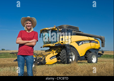 Un adolescente ragazza di fattoria di fronte a una mietitrebbia durante il raccolto di canola, Tiger colline, Manitoba, Canada Foto Stock