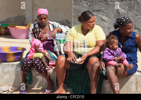 Sal Rei Boa Vista Capo Verde tre donne locali seduti fuori con una madre che dà la sua bambina una bevanda di acqua in bottiglia. Foto Stock