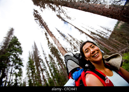 Una madre porta in sé il figlio in un bambino zaino lungo la Williams Creek Trail, mentre si dorme. Gli alberi morti salire al di sopra di un passato f Foto Stock