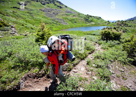 Una donna escursioni al di sopra della linea di albero su Williams Creek Trail (sentiero numero 587) mentre si sta portando il suo Figlio nel suo zaino. Foto Stock