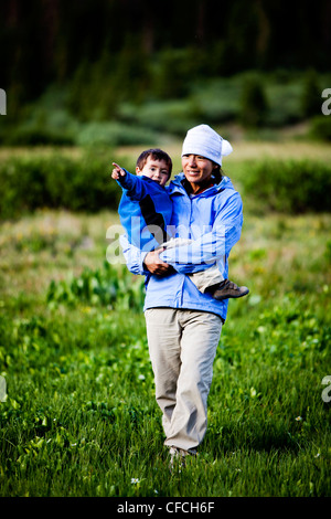 Una donna cammina attraverso un prato presso Squaw Pass mentre tiene il suo figlio di 2 anni. Foto Stock