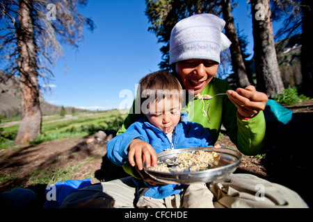 Un ragazzo si siede sul suo madri giro mentre mangiano gli spaghetti nel backcountry. Essi sono accampati presso Squaw Pass. Foto Stock