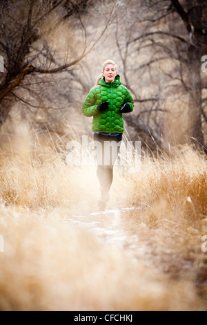 Una giovane donna corre un sentiero verso il basso attraverso l'erba Morta appena a nord di Dixon serbatoio, in un freddo giorno di un verde down jacket. Foto Stock