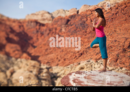 Montare una giovane donna asiatica a praticare yoga durante una scalata su roccia viaggio, Red Rocks, Las Vegas, Nevada, Stati Uniti d'America Foto Stock