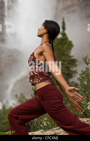 Giovane donna pratica lo yoga sotto le cascate di Takakkaw nel Parco Nazionale di Yoho, campo, British Columbia, Canada Foto Stock