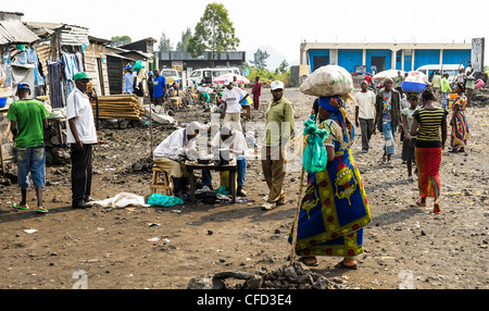 Una strada trafficata scena a Goma, le donne che trasportano merci pesanti mentre gli uomini riparare i prodotti elettronici. Foto di Julie Edwards Foto Stock
