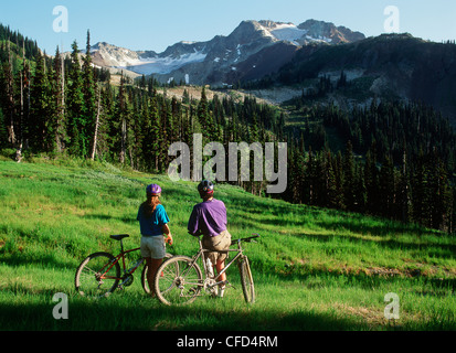 Coppia giovane resto in bici in prato, Whistler picco, British Columbia, Canada. Foto Stock