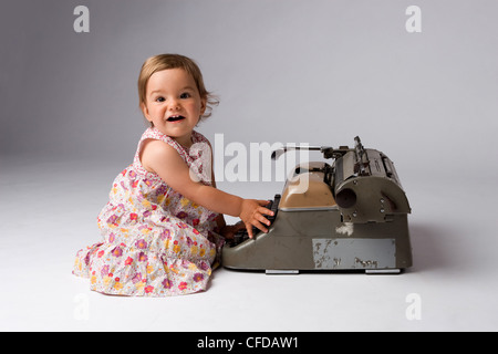 Carino gioiosa bambina divertendosi con una macchina da scrivere di antiquariato. Foto Stock