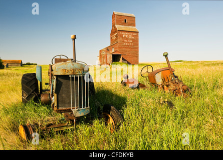 I vecchi trattori con elevatore granella in background, abbandonata città di Bents, Saskatchewan, Canada Foto Stock