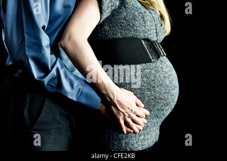 Una immagine di maternità di una coppia contro una chiave di basso, sfondo nero, raffigurato dalle spalle ai fianchi soltanto. Foto Stock