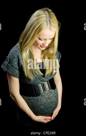 Una immagine di maternità di una bella donna bionda, contro una chiave di basso (nero) sullo sfondo. Foto Stock