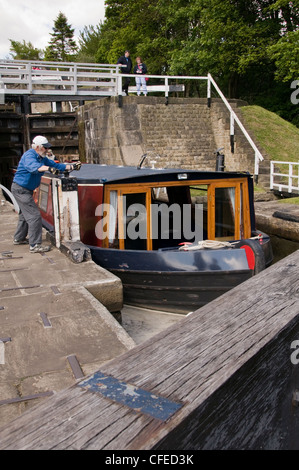 Narrowboat nella camera di bloccaggio passando attraverso l'aumento di cinque serrature su Leeds Liverpool Canal (avvolgimento man maniglie per sollevare il portellone paddle) - Bingley, Inghilterra. Foto Stock