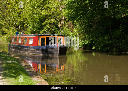 Narrowboat viaggiando lungo il panoramico soleggiato tratto rurale di acqua (Leeds Liverpool Canal) con coppia a bordo - Bingley, West Yorkshire, Inghilterra, Regno Unito Foto Stock