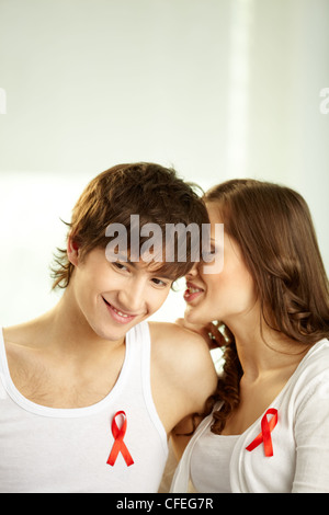 Ragazza whispering alcuni segreti nel suo fidanzato l orecchio, nastri rossi attaccati al loro abbigliamento Foto Stock