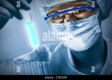 Masked donna scienziato in bicchieri studiando un campione di luminosa Foto Stock