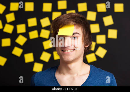 Felice studente con un promemoria sulla testa e con più carta gialla note in background Foto Stock