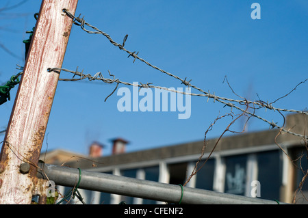 Una sezione di filo spinato di fronte ad un edificio abbandonato Foto Stock