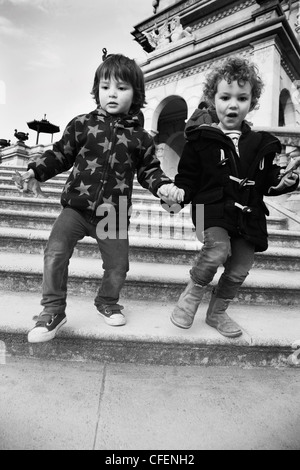 Due 3 anno old boys camminando mano nella mano lungo la scalinata in pietra. Foto Stock