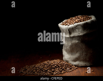 Sacco di tela di chicchi di caffè scuro contro uno sfondo di legno Foto Stock