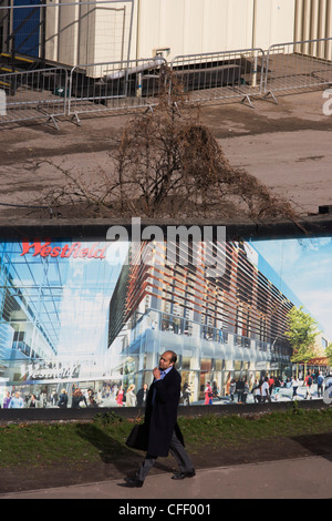 Comunità locale passa una palizzata che mostra l'aspirazione e il consumismo della vicina città di Westfield Shopping Complex, Stratford. Foto Stock