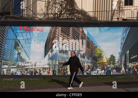 Comunità locale passa una palizzata che mostra l'aspirazione e il consumismo della vicina città di Westfield Shopping Complex, Stratford. Foto Stock