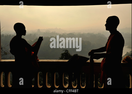 I monaci buddisti, novizi, rivestimento le loro vesti, vista da est, su alberi e colline in polvere di mattina, l'unità Phu Si Hill, Luang Prabang Foto Stock