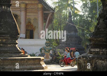 Le donne su scooter all'interno di un tempio composto con chedis, Luang Prabang, Laos, Repubblica Democratica Popolare del Laos Foto Stock