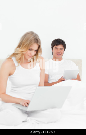 Uomo che guarda in avanti e sorridente come egli utilizza una tavoletta, mentre lei utilizza un laptop Foto Stock