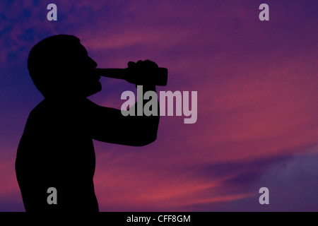 Un surfista maschio beve una birra guardando il tramonto dopo una lunga giornata di navigazione a Pasquales, Messico. Foto Stock