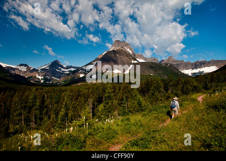 Un vecchio uomo cammina lungo un periodo di prova nel mezzo della giornata su un cielo blu chiaro giorno con una montagna di distanza. Foto Stock