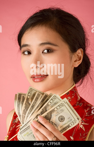 Ritratto di giovane donna Cinese in abiti tradizionali (cheongsam) azienda pila di noi carta moneta di venti dollari fatture Foto Stock